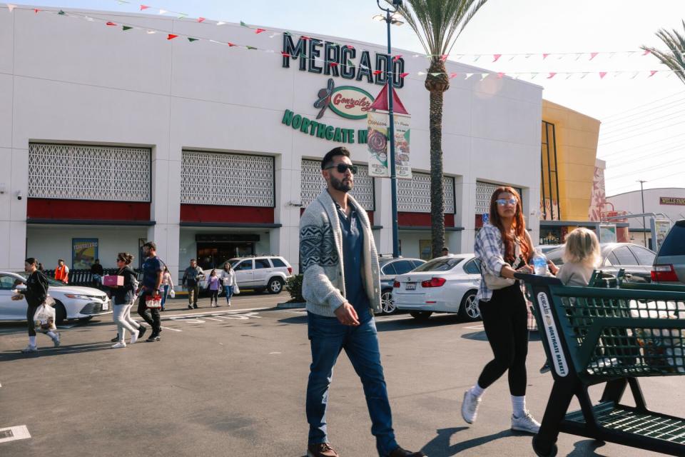 Two people push a shopping cart in the parking lot in front of Mercado González Northgate Market.