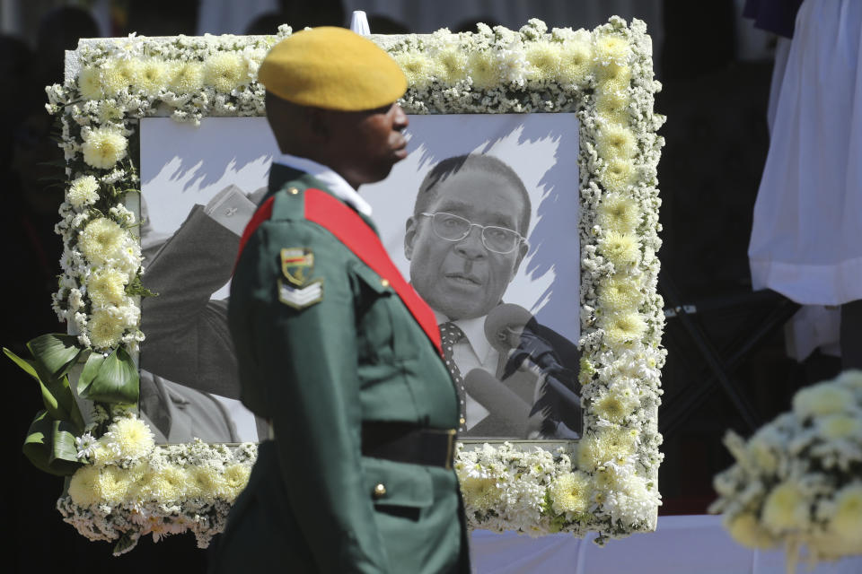 A soldier stands next to a portrait of former Zimbabwean President Robert Mugabe during mass at his rural home in Zvimba, about 100 kilometers north west of the capital Harare, Saturday. Sept, 28, 2019. According to a family spokesperson Mugabe is expected to be buried at the residence after weeks of drama mystery and contention over his burial place. (AP Photo/Tsvangirayi Mukwazhi)