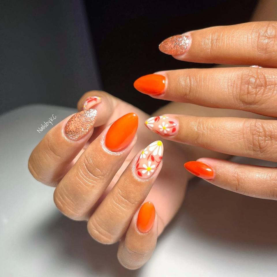 Match your mani to the orange and crimson foliage with this adorable design. All you need to emulate the look is some orange polish like <a href="https://www.amazon.com/essie-polish-Handmade-collection-pumpkin/dp/B09YZ2NPJB/r" rel="nofollow noopener" target="_blank" data-ylk="slk:Essie's To DIY For;elm:context_link;itc:0;sec:content-canvas" class="link ">Essie's To DIY For</a>, <a href="https://www.amazon.com/Sally-Hansen-Treatment-Shimmer-Twinkle/dp/B00KE4ELUM/" rel="nofollow noopener" target="_blank" data-ylk="slk:shimmer topcoat;elm:context_link;itc:0;sec:content-canvas" class="link ">shimmer topcoat</a>, and <a href="https://www.glamour.com/gallery/flower-nail-art-designs?mbid=synd_yahoo_rss" rel="nofollow noopener" target="_blank" data-ylk="slk:floral nail decals;elm:context_link;itc:0;sec:content-canvas" class="link ">floral nail decals</a>.