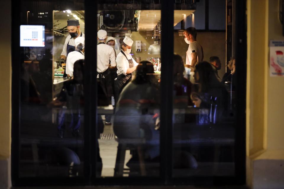 Waiters wearing in face masks and gloves to protect against coronavirus serve customers siting inside a restaurant at Patriarshiye Prudy, a hip restaurant and bar district in Moscow, Russia, late Friday, Oct. 16, 2020. The outbreak in Russia this month is breaking the records set in the spring, when a lockdown to slow the spread was put in place. But, as governments across Europe move to reimpose restrictions to counter rising cases, authorities in Russia are resisting shutting down businesses again. (AP Photo/Alexander Zemlianichenko)