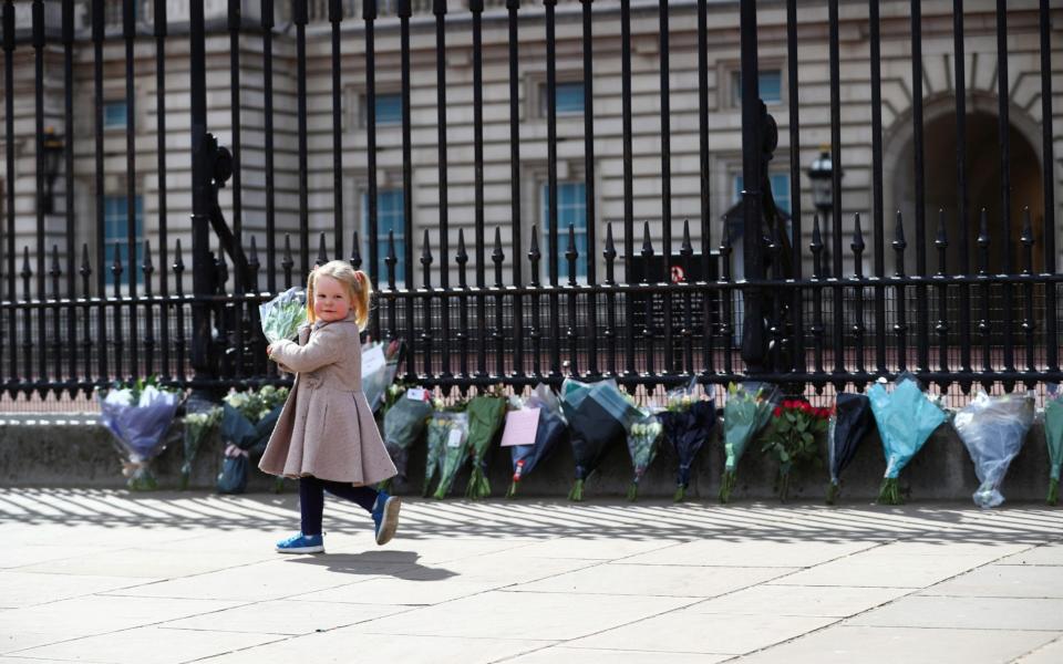 Maggie, 2, lays down a bouquet of flowers outside Buckingham Palace after it was announced that Britain's Prince Philip, husband of Queen Elizabeth, has died at the age of 99, - Hannah McKay/ Reuters 