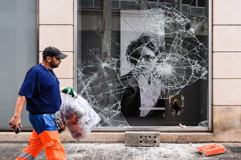 Un empleado municipal trabaja frente a una tienda saqueada tras la cuarta noche consecutiva de disturbios en Francia provocados por la muerte del conductor adolescente Nahel por una bala de la policía, en Lyon, sureste de Francia, el 1 de julio de 2023.