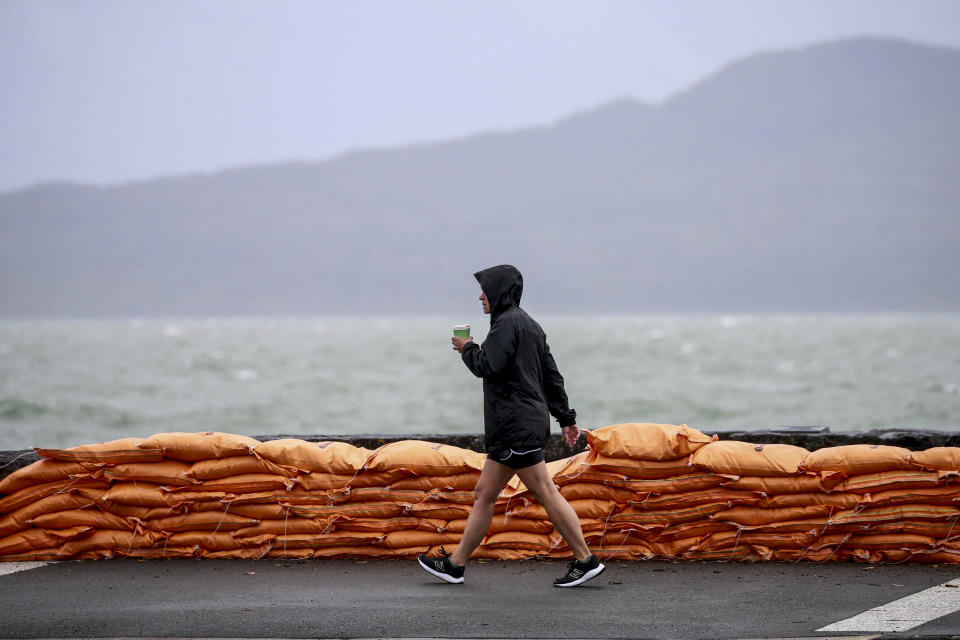 A man walks past sand bags along the waterfront in Auckland, New Zealand, Sunday, Feb. 12, 2023. New Zealand's national carrier has canceled dozens of flights as Aucklanders brace for a deluge from Cyclone Gabrielle, two weeks after a record-breaking storm swamped the nation's largest city and killed several people. (Alex Burton/NZ Herald via AP)