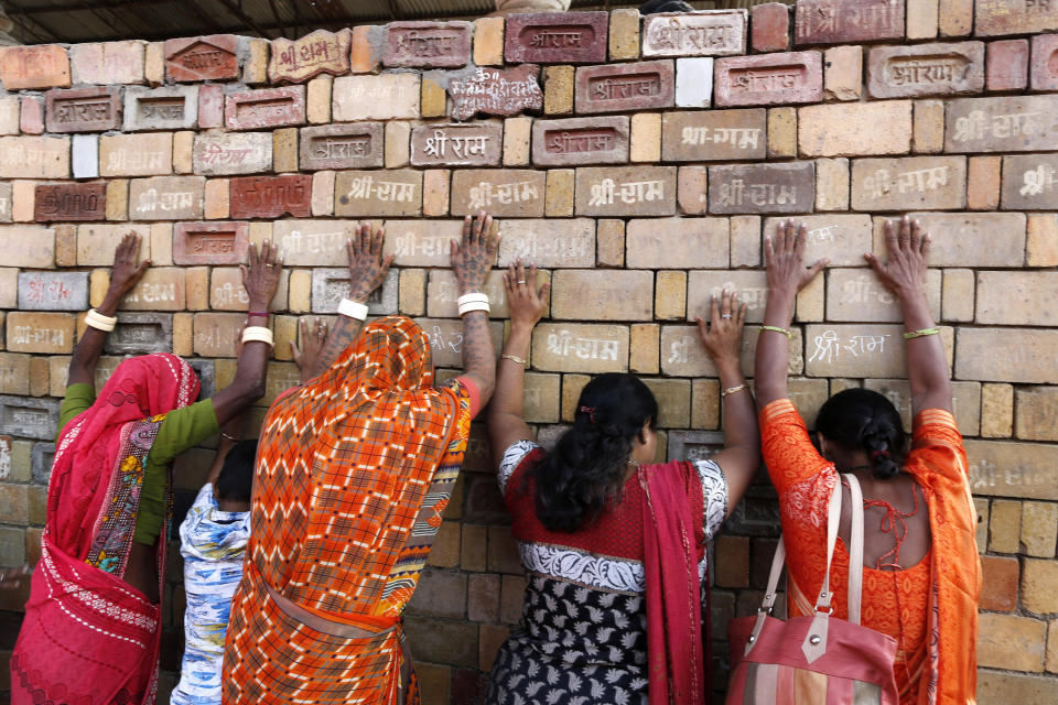 FILE- In this Nov. 11, 2019 file photo, Hindu women devotees pray to the bricks reading "Shree Ram" ( Lord Ram), which are expected to be used in constructing Ram temple, in Ayodhya, India. India’s Prime Minister Narendra Modi will attend a groundbreaking ceremony next month for a Hindu temple on a disputed site in northern India where a 16th-century mosque was torn down by Hindu hard-liners in 1992. The trust overseeing the temple construction says the ceremony is set for Aug. 5, a date they say is astrologically auspicious for Hindus but that also marks a year since the Indian Parliament revoked the semi-autonomous status of its only Muslim-majority state, Jammu and Kashmir. (AP Photo/Rajesh Kumar Singh, File)