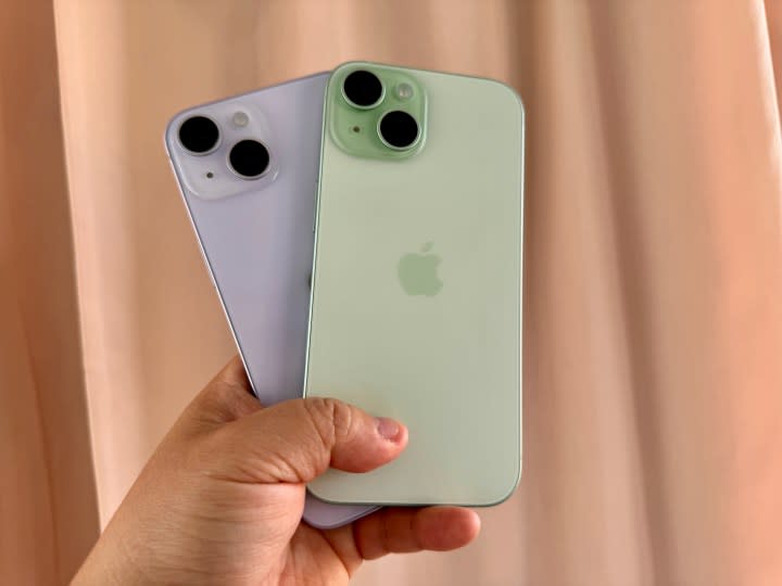 Purple iPhone 14 (left) and a green iPhone 15 in hand.