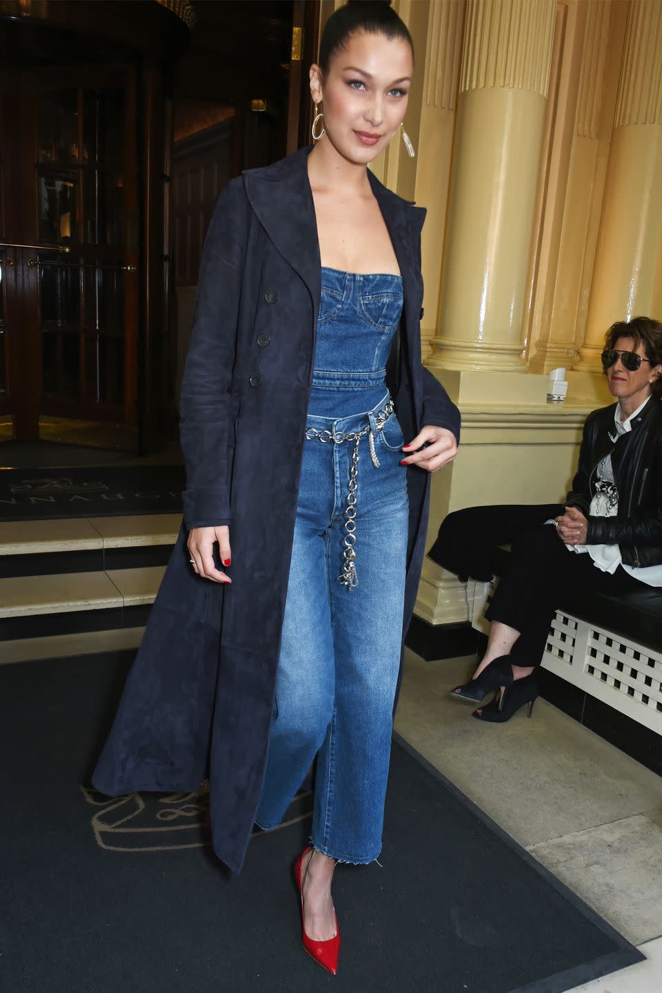 <p>In a navy blue suede trench coat, denim bustier and cropped jeans, chain belt, red pumps and statement earrings at a Dior launch event in London.</p>