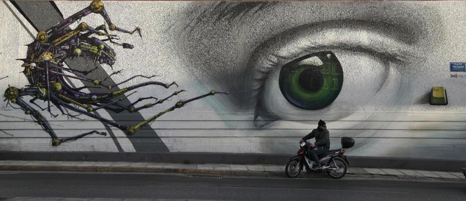 In this photo taken on Thursday Feb. 20, 2014, a motorcyclist passes the work 'Access Control' by Greek street artist iNO, on central Pireos Street in Athens. Greece has attracted international street artists to its capital, due to the availability of commissioned work and relatively lax anti-graffiti law. (AP Photo/Dimitri Messinis)