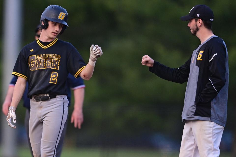 Garfield's Brandyn Bogucki is congratulated by the first-base coach after hitting an RBI single during the fifth inning against Kirtland in an OHSAA district semifinal Monday night at Cene Park in Struthers.