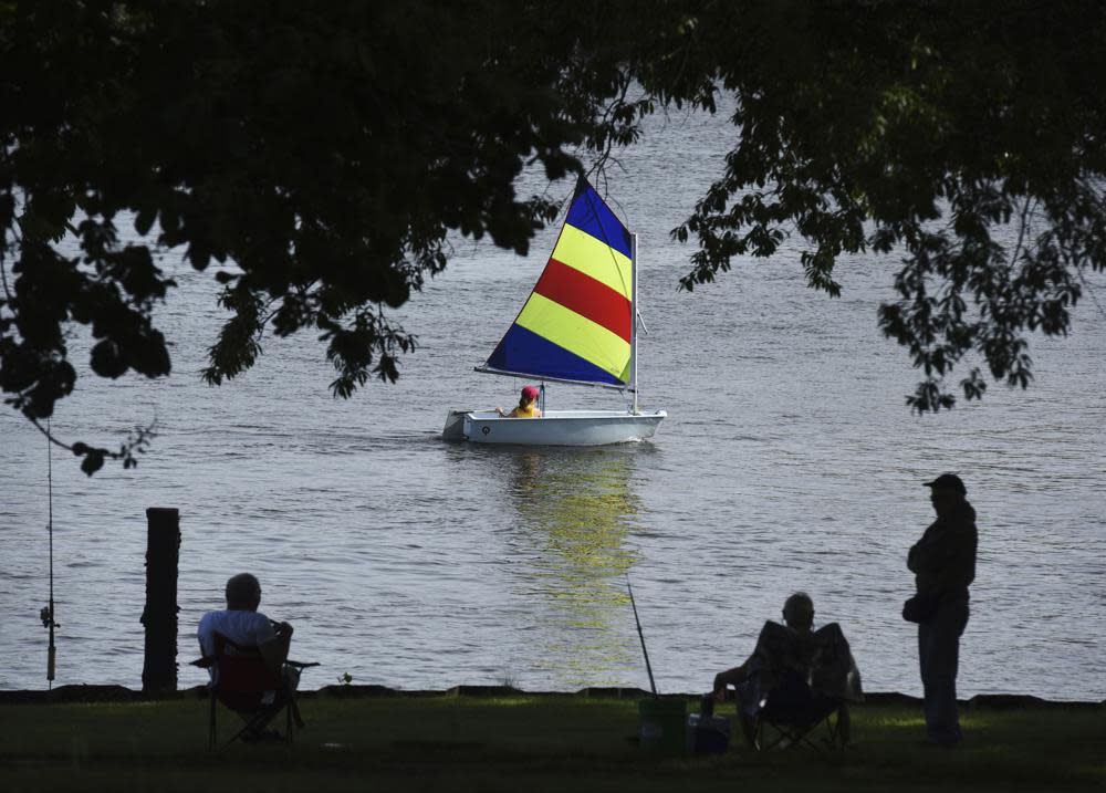 FILE – A sailor with the St. Joseph Junior Foundation Summer Sailling School cruises past fishermen along the St. Joseph River in St. Joseph, Mich., Wednesday, June 15, 2022. The fast-changing coronavirus has kicked off summer in the U.S. with lots of infections but relatively few deaths compared to its prior incarnations. COVID-19 is still killing hundreds of Americans each day, but for many people the virus is not nearly as dangerous as it was. (Don Campbell/The Herald-Palladium via AP)