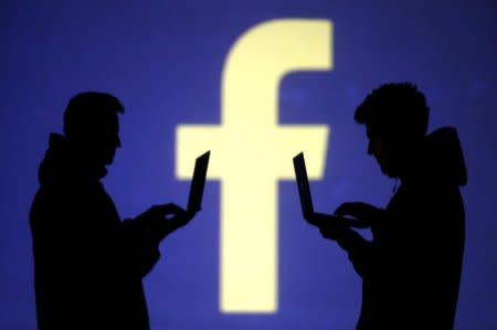 FILE PHOTO - Silhouettes of laptop users are seen next to a screen projection of Facebook logo in this picture illustration taken March 28, 2018.  REUTERS/Dado Ruvic/Illustration