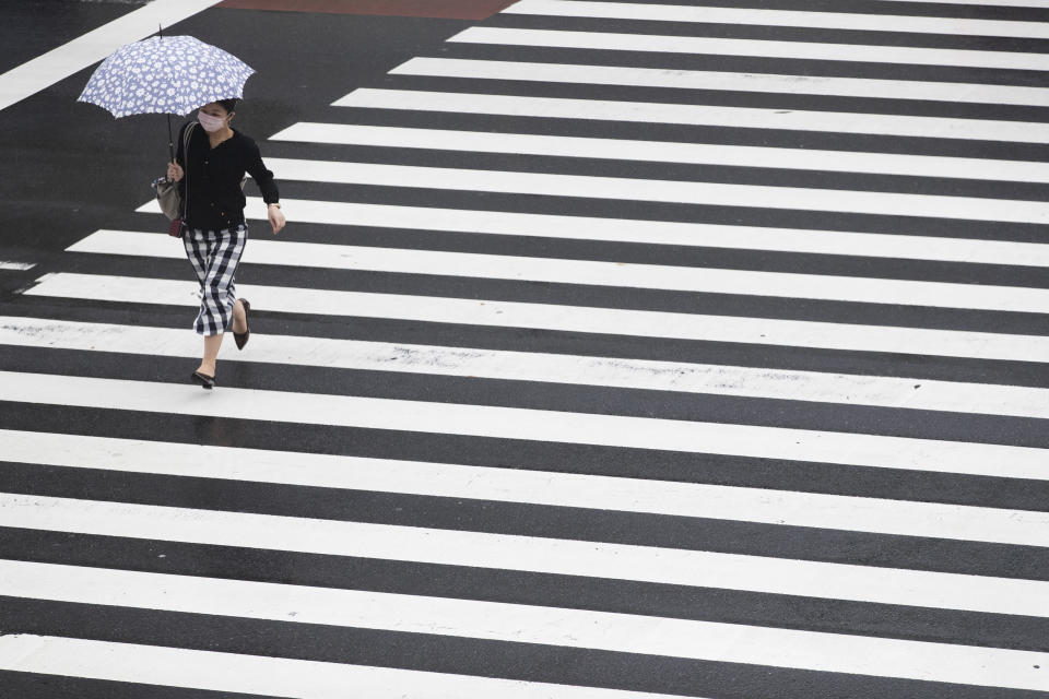 A woman wearing a face mask to help curb the spread of the coronavirus walks across an intersection in a drizzle in Tokyo, Thursday, Sept. 2, 2021. (AP Photo/Hiro Komae)