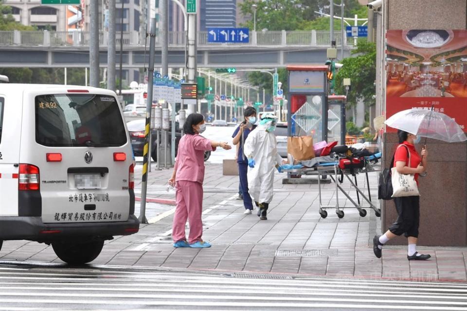 染疫者在家中、集中檢疫所猝死狀況頻傳，疫情指揮中心擬訂新版分流規定，未來只有60歲以下、無慢性病的患者才能居家隔離。圖為台北市一處防疫旅館，病患在醫護人員安全護送下，自防疫旅館內移出，由救護車送往醫院。（中央社）