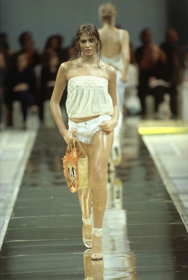 Ein Model auf dem Laufsteg der Frühling/Sommer 2000 Chloé Ready-To-Wear-Kollection, die von Stella McCartney entworfen wurde. Zu einem weißen Schlauchtop mit Faltenrand und zerrissenen Hotpants trägt sie hochhackige Sandalen mit weißen und goldenen Riemchen und einen Strohbeutel mit Katzengesicht. (Bild: Getty Images)