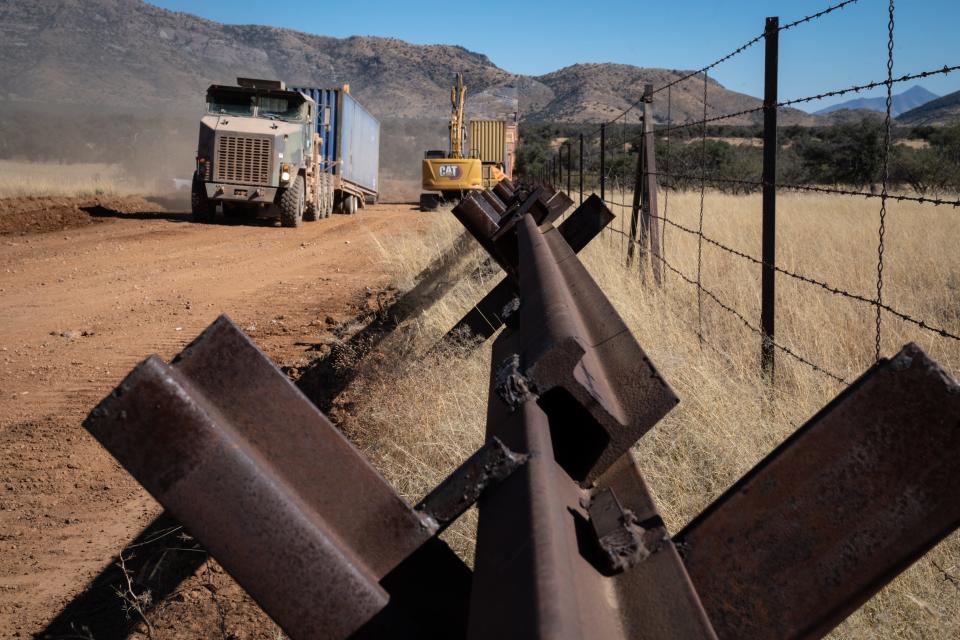 A shipping container (left) is transported for the wall being built on the U.S./Mexico border on Nov. 18, 2022, southwest of Sierra Vista, Arizona. A doubled-stacked shipping container wall (back center) is replacing the Normandy vehicle barriers (foreground).