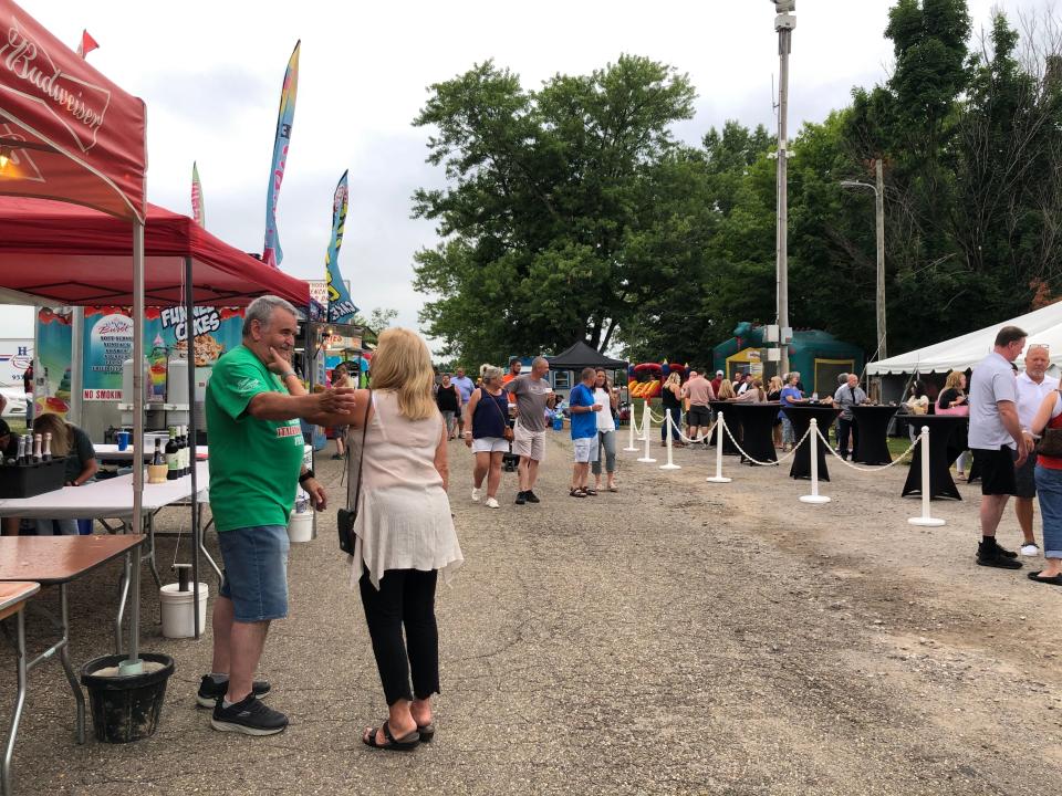 Mike Henderhand, a volunteer for the Stark County Italian-American Festival, greets a friend while staffing the beer table at the festival in Weis Park in Canton Friday evening.