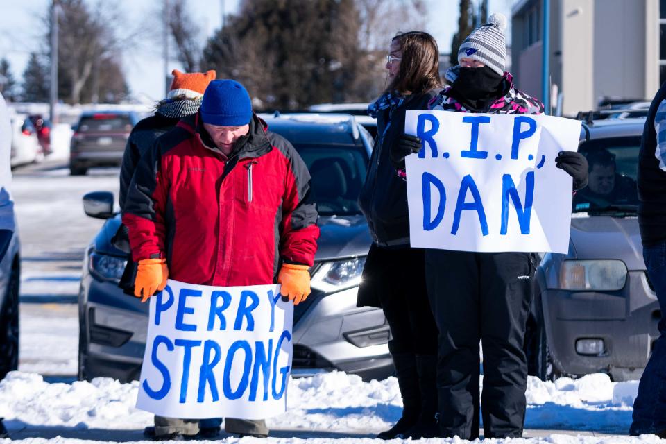 Perry educators Gary Overla, left, and Brenda Mintun hold signs as they wait for the hearse bearing the body of Principal Dan Marburger Tuesday, Jan. 16, 2024, in Perry.