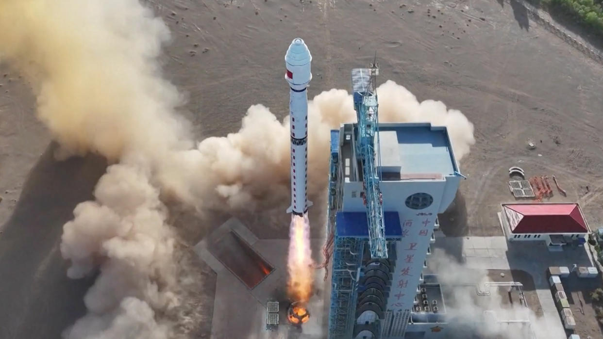  A white rocket lifts off in the desert above a cloud of dust and smoke. 