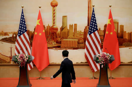 FILE PHOTO: A staff member walks past U.S. and Chinese flags placed for a joint news conference by U.S. Secretary of State Mike Pompeo and Chinese Foreign Minister Wang Yi at the Great Hall of the People in Beijing, China June 14, 2018. REUTERS/Jason Lee/File Photo