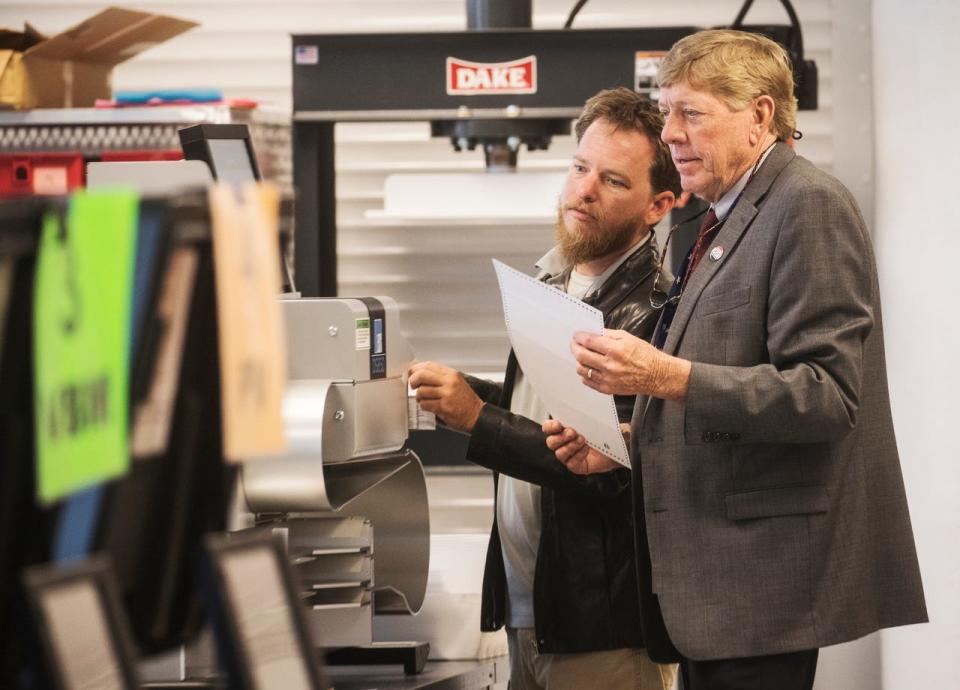 Russ Bryan, network security specialist left, and Tommy Doyle, right, the Supervisor of Elections for the Lee County Supervisor of Elections feeds votes into a vote-by-mail tabulator at the Lee County Elections main office in 2020.