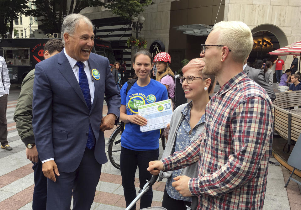 FILE - In this June 28, 2018, file photo in Seattle Wash., Washington Gov. Jay Inslee speaks to people as he helps to gather signatures for a proposed initiative that would charge large industrial emitters a fee for their carbon emissions. Voters in Washington state will be asked this fall to do what state and federal leaders have been reluctant to: charge a direct fee on carbon pollution to fight climate change. If the measure passes, it will be the first direct fee or tax charged on carbon emissions in the U.S. Experts say it will show that states can take climate action even if the Trump administration doesn't and nudge other states to follow. (AP Photo/Phuong Le, File)