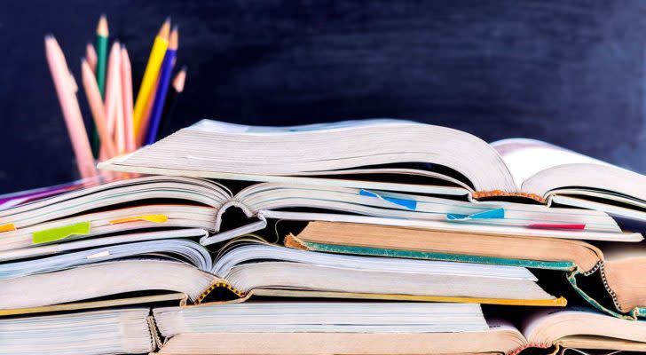 A stack of open textbooks on a table in front of a chalkboard background.