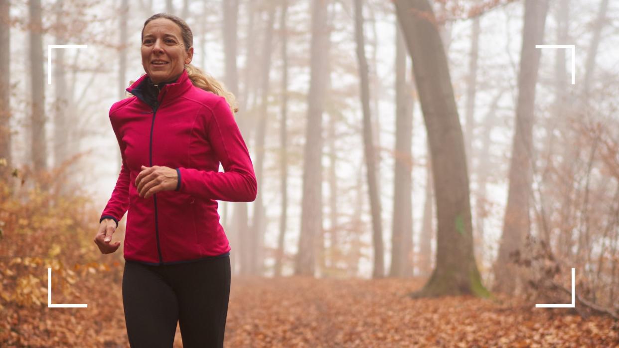  Woman running along path with autumn leaves on the ground in workout gear after learning how to work out in cold weather. 