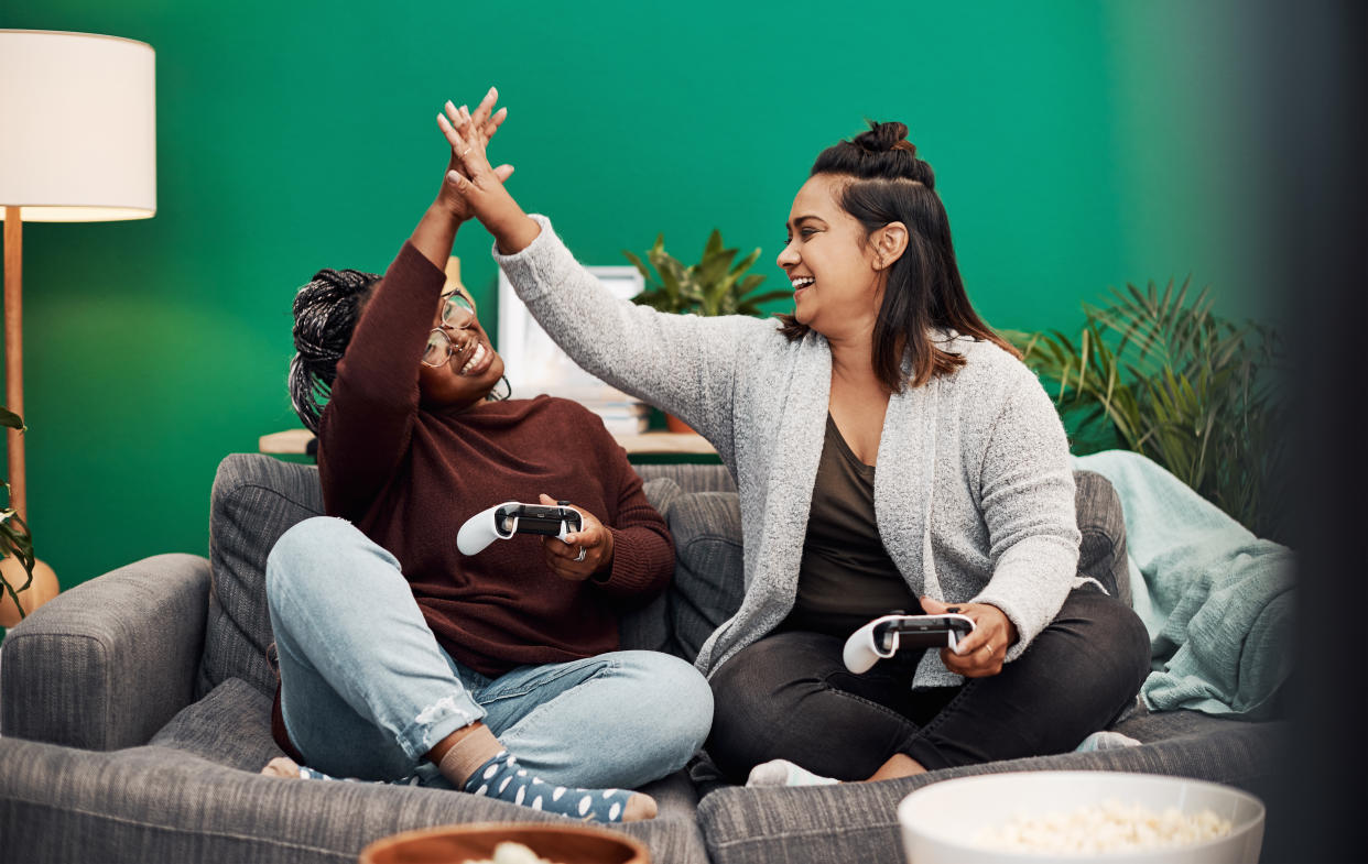 Shot of two young women giving each other a high five while playing video games on the sofa at home