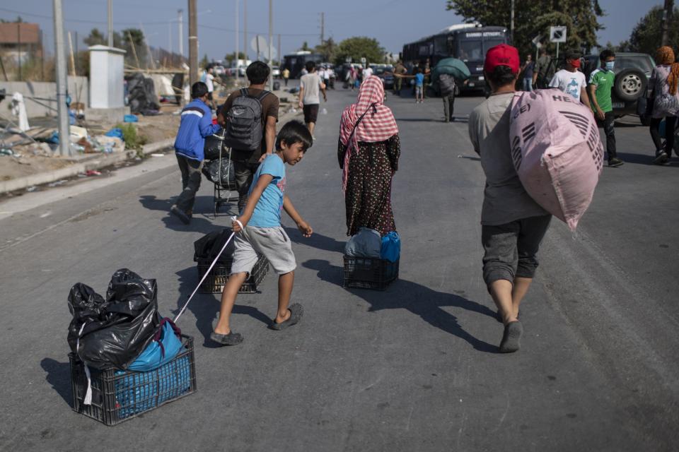 Migrants pull their belongings as they walk to the new temporary refugee camp in Kara Tepe, near Mytilene the capital of the northeastern island of Lesbos, Greece, Thursday, Sept. 17, 2020. Greek police are moving hundreds of migrants to an army-built camp on the island of Lesbos Thursday after a fire destroyed an overcrowded facility, leaving them homeless for days. (AP Photo/Petros Giannakouris)