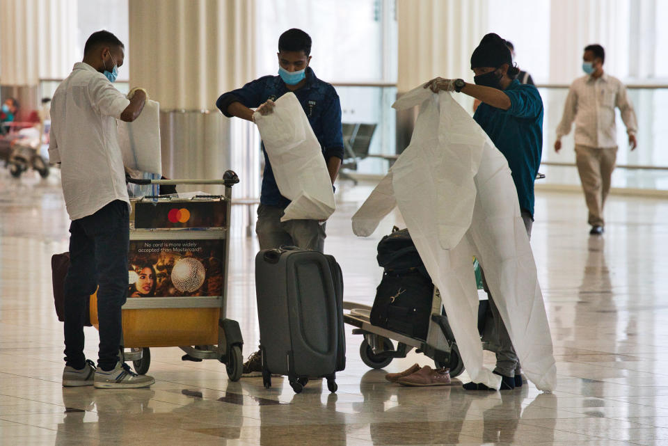 Passengers wearing masks due to the coronavirus pandemic put on throwaway coveralls before their flight at Dubai International Airport's Terminal 3 in Dubai, United Arab Emirates, Wednesday, June 10, 2020. The coronavirus pandemic has hit global aviation hard, particularly at Dubai International Airport, the world's busiest for international travel, due to restrictions on global movement over the virus. (AP Photo/Jon Gambrell)