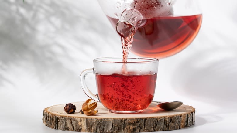 A pitcher pouring hibiscus tea into a glass mug