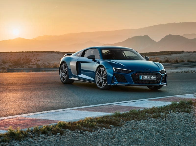 An Audi R8 parked on a race track in front of a gorgeous sunset silhouetting the mountains.