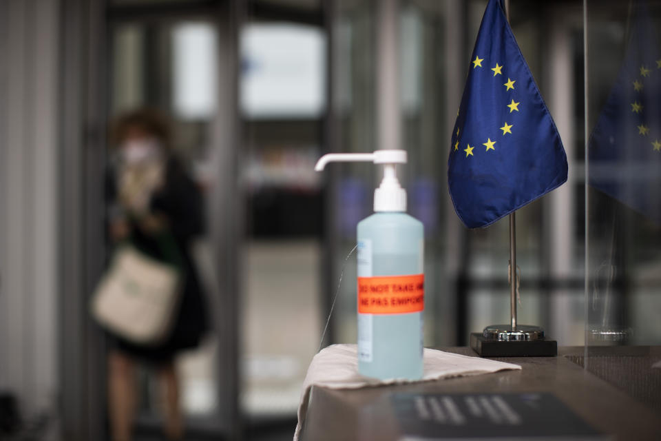 A bottle of hand sanitizer stands next to an EU flag at the entrance to the European Council building in Brussels, Thursday, July 16, 2020. On Friday, July 17, 2020, leaders from the 27 European Union nations will meet face-to-face to try to carve up a potential package of 1.85 trillion euros among themselves. Due to coronavirus concerns, Friday's summit will be held in a larger-than-usual meeting room to meet social distancing requirements, the media will be kept to a minimum and there will be no group photo of the leaders. (AP Photo/Francisco Seco)
