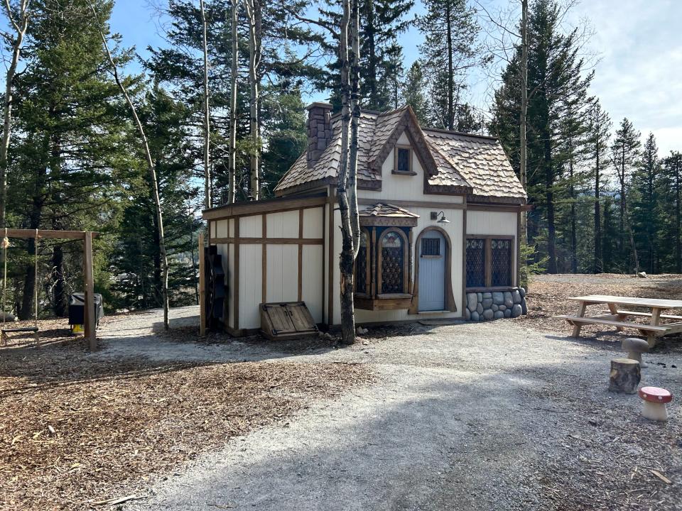 belle's cottage with blue doors, simple paneling. surrounded by trees with swing next to it