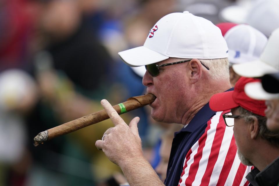 A fan smokes a large cigar on the 10th hole during a practice day at the Ryder Cup at the Whistling Straits Golf Course Wednesday, Sept. 22, 2021, in Sheboygan, Wis. (AP Photo/Ashley Landis)