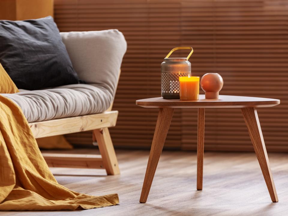 A couch with a yellow throw and gray pillow beside an end table with candles