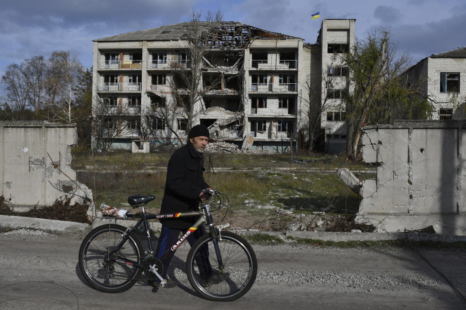 A man with a bicycle passes a building damaged by shellings in the liberated village of Shchurove, Donetsk region, Ukraine, Monday, Nov. 7, 2022. (AP Photo/Andriy Andriyenko)