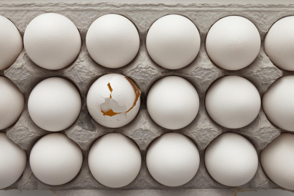 an overhead shot of a carton of white eggs, one of which is broken