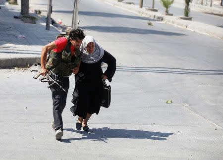 FILE PHOTO: A Free Syrian Army fighter helps a woman to run across a street during clashes in Aleppo, Syria August 12, 2012. REUTERS/Goran Tomasevic/File Photo