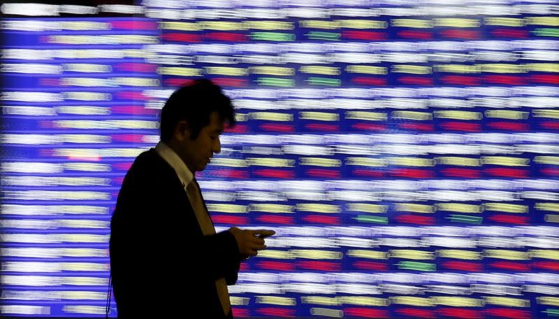 A man, holding a mobile phone, walks past an electronic stock quotation board outside a brokerage in Tokyo, Japan, December 1, 2015. REUTERS/Toru Hanai