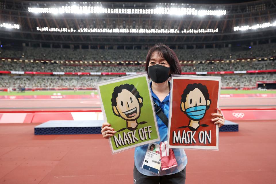A photo team member holds Mask Off and Mask On signage at the Tokyo Olympics.
