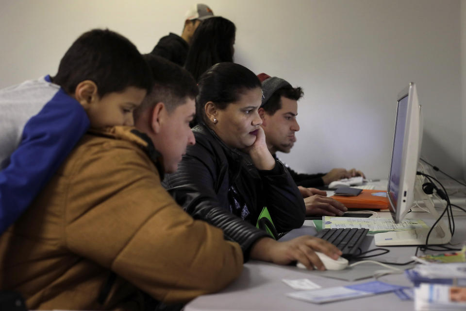 In this Wednesday, Dec. 4, 2019 photo Helison Alvarenga, of Brazil, second from left, sits with his 6-year-old son, David, left, and 24-year-old wife, Amanda, center, as they use a computer monitor while pursuing replacement passports at the New England Community Center, in Stoughton, Mass. Alvarenga, a 26-year-old from the Brazilian state of Minas Gerais, arrived in Massachusetts about four months ago after crossing the Mexican border at Juarez with his family. The three were at the community center Dec. 4, to apply for new Brazilian passports, which Alvarenga says were seized by border officials. (AP Photo/Steven Senne)