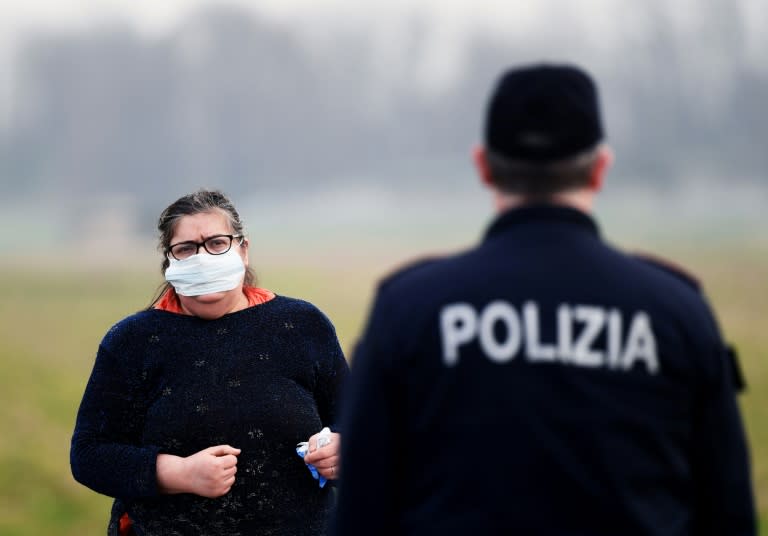 A resident wearing a respiratory mask (L) talks with a police officer at the entrance to the town of Casalpusterlengo, southeast of Milan, an area where most of Italy's new-coronavirus cases have emerged