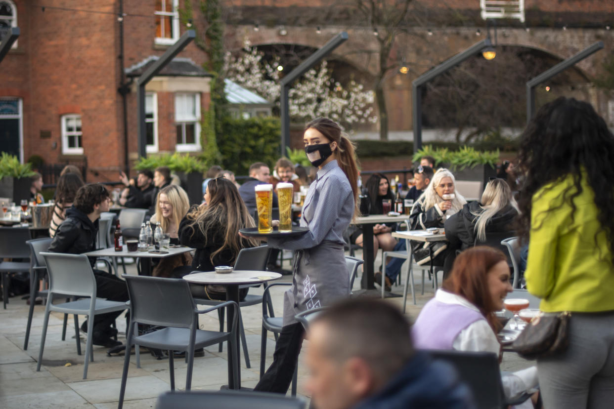 MANCHESTER, ENGLAND - APRIL 12: A waitress carries a tray of drinks in the beer garden at Dukes 92 bar on April 12, 2021 in Manchester, England. England has taken a significant step in easing its lockdown restrictions, with non-essential retail, beauty services, gyms and outdoor entertainment venues among the businesses given the green light to re-open with coronavirus precautions in place. Pubs and restaurants are also allowed open their outdoor areas, with no requirements for patrons to order food when buying alcoholic drinks. (Photo by Anthony Devlin/Getty Images)