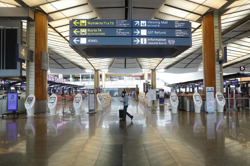 SINGAPORE - MARCH 24:  An airport staff wearing protective mask walks past an empty self check in kiosk at the departure terminal at Changi Airport on March 24, 2020 in Singapore. Singapore will not allow short term visitors to enter or transit through the country from March 24 to contain the spread of the imported COVID-19  infection.  (Photo by Suhaimi Abdullah/Getty Images)