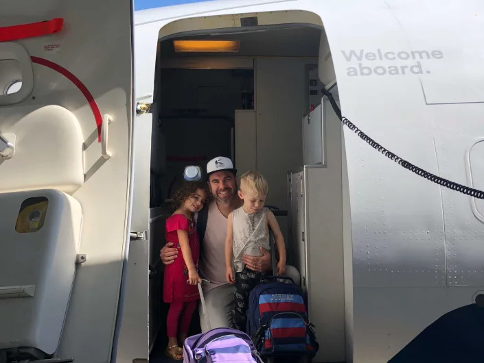 A man and two children posing at an airplane door.
