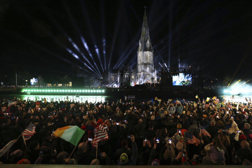 People watch a large screen showing President Joe Biden speaking outside St Muredach's Cathedral, in Ballina, Ireland, Friday, April 14, 2023. (AP Photo/Peter Morrison)