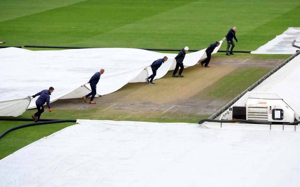 Ground staff bring out the covers as rain delays the start of day two