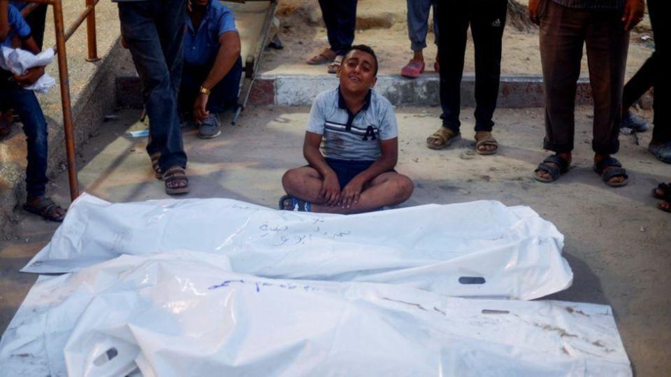 Un niño llora frente a cadáveres envueltos en bolsas de plástico