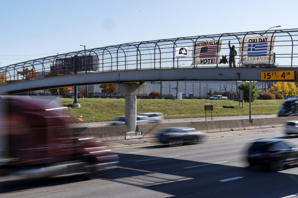 An Iraq and Afghanistan war veteran, who did not give his name, stands on a highway overpass with signs encouraging motorists to vote in Hamtramck, Mich., Wed, Oct. 28, 2020. Early voting numbers, nearly 90 million by Saturday morning, suggest 2020 will shatter voter turn-out records. Trump has alleged without evidence that wide-spread absentee voting will lead to fraud. (AP Photo/David Goldman)