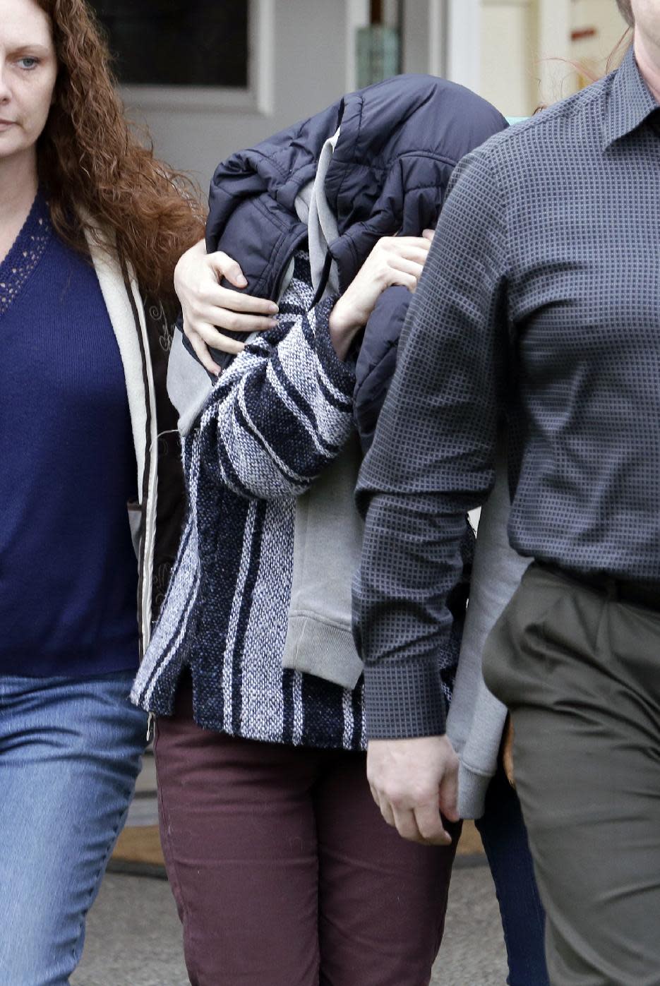 ADDS STATEMENT FROM KNOX SPOKESMAN DAVID MARRIOTT-An unidentified woman, center, is hidden under a jacket while being escorted from the home of Amanda Knox's mother, Thursday, Jan. 30, 2014, in Seattle. Knox’s family spokesman, David Marriott, said Thursday that Knox was at the house when an Italian court upholding her murder conviction was read Thursday, but said he didn’t know whether the person who emerged was Knox. On Friday, Marriott stated he had made inquiries and that the person under the jacket wasn’t Knox. (AP Photo)